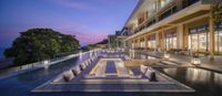 an outdoor pool is lit up at dusk overlooking a resort with large balconies on the edge