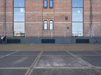 empty parking lot in front of brick building with a metal fence and a person sitting on a bench