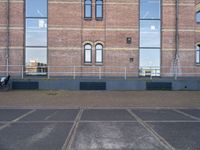 empty parking lot in front of brick building with a metal fence and a person sitting on a bench