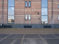 empty parking lot in front of brick building with a metal fence and a person sitting on a bench