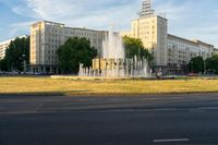 a water fountain and fountain statue in front of a tall building with trees near by