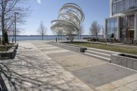 a sculpture is set beside the water's edge at a lakefront area with benches on either side