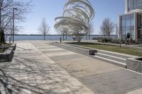 a sculpture is set beside the water's edge at a lakefront area with benches on either side