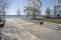 a sculpture is set beside the water's edge at a lakefront area with benches on either side