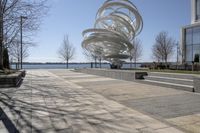 a sculpture is set beside the water's edge at a lakefront area with benches on either side