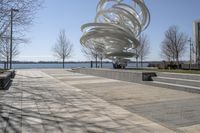 a sculpture is set beside the water's edge at a lakefront area with benches on either side