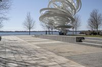 a sculpture is set beside the water's edge at a lakefront area with benches on either side