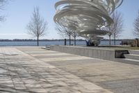 a sculpture is set beside the water's edge at a lakefront area with benches on either side