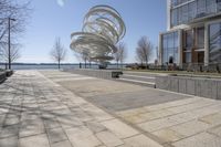 a sculpture is set beside the water's edge at a lakefront area with benches on either side