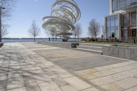 a sculpture is set beside the water's edge at a lakefront area with benches on either side