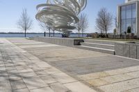 a sculpture is set beside the water's edge at a lakefront area with benches on either side