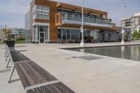 wooden benches sit near a water front and patio area next to the building and patio