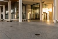 a paved sidewalk with concrete steps leading into a large building with glass doors and doors on either side