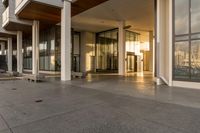 a paved sidewalk with concrete steps leading into a large building with glass doors and doors on either side