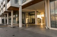 a paved sidewalk with concrete steps leading into a large building with glass doors and doors on either side