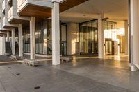 a paved sidewalk with concrete steps leading into a large building with glass doors and doors on either side