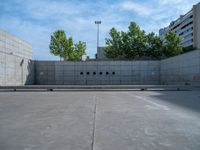 the empty parking lot in front of a wall with apartment buildings on it and a skateboarder on a ramp