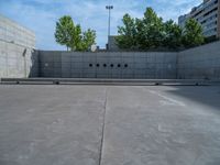 the empty parking lot in front of a wall with apartment buildings on it and a skateboarder on a ramp