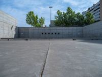 the empty parking lot in front of a wall with apartment buildings on it and a skateboarder on a ramp