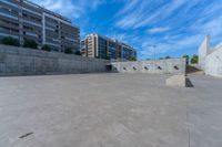 the empty parking lot in front of a wall with apartment buildings on it and a skateboarder on a ramp