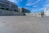 the empty parking lot in front of a wall with apartment buildings on it and a skateboarder on a ramp