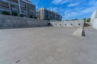 the empty parking lot in front of a wall with apartment buildings on it and a skateboarder on a ramp