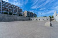 the empty parking lot in front of a wall with apartment buildings on it and a skateboarder on a ramp