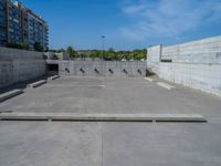 the empty parking lot in front of a wall with apartment buildings on it and a skateboarder on a ramp