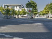 empty street in a city with many tall buildings and green trees surrounding it a road sign with a crosswalk, a sign that says don't stop is empty, street signs are on a street is next to them