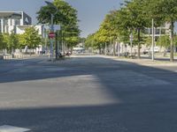 empty street in a city with many tall buildings and green trees surrounding it a road sign with a crosswalk, a sign that says don't stop is empty, street signs are on a street is next to them