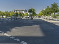 empty street in a city with many tall buildings and green trees surrounding it a road sign with a crosswalk, a sign that says don't stop is empty, street signs are on a street is next to them