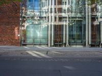 a grey car sitting next to a building with glass walls and doors and a tree