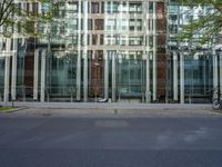 a grey car sitting next to a building with glass walls and doors and a tree