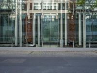 a grey car sitting next to a building with glass walls and doors and a tree