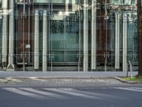 a grey car sitting next to a building with glass walls and doors and a tree