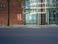 a grey car sitting next to a building with glass walls and doors and a tree