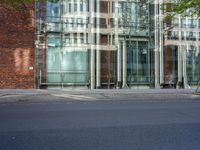 a grey car sitting next to a building with glass walls and doors and a tree