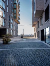 brick walkway with stone pavers along two sides near two tall buildings and the sea in the distance