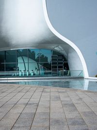 a black umbrella stands in front of the water - filled pool of a building with windows