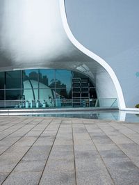 a black umbrella stands in front of the water - filled pool of a building with windows