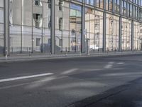 a large building is reflected in the side of the street that goes along this narrow road