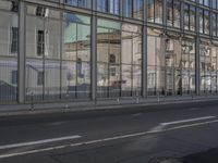 a large building is reflected in the side of the street that goes along this narrow road