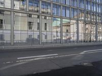 a large building is reflected in the side of the street that goes along this narrow road