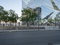 a large glass building with trees in front of it and people walking down the sidewalk