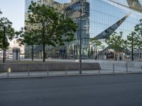 a large glass building with trees in front of it and people walking down the sidewalk