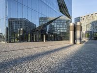 buildings reflected in glass with two metal pillars on brick ground in front of them with reflection of other buildings