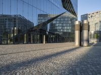 buildings reflected in glass with two metal pillars on brick ground in front of them with reflection of other buildings