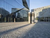 buildings reflected in glass with two metal pillars on brick ground in front of them with reflection of other buildings