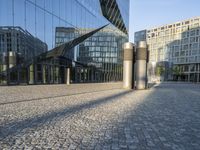 buildings reflected in glass with two metal pillars on brick ground in front of them with reflection of other buildings