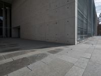 a concrete building with some windows next to some brick paving and stone ground with a bench in front